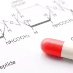 Czerwono-biała kapsułka leży obok wzoru chemicznego. Może to być związane z testem na narkotyki lub badaniami nad nowymi lekami.