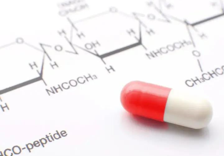 Czerwono-biała kapsułka leży obok wzoru chemicznego. Może to być związane z testem na narkotyki lub badaniami nad nowymi lekami.