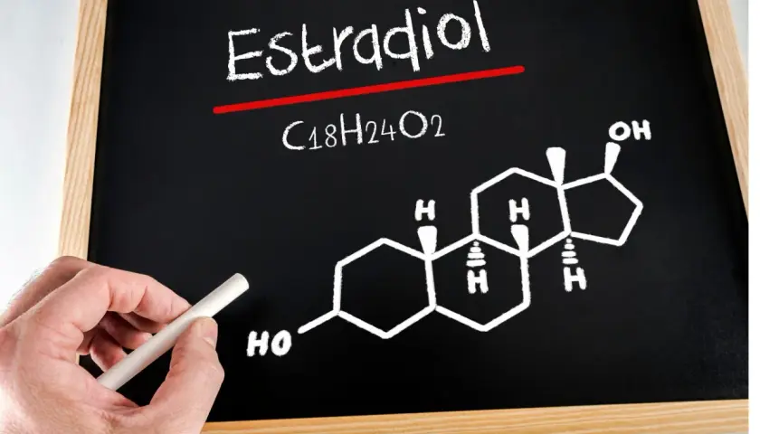 Tablica z napisem "Estradiol" i jego wzorem chemicznym C18H24O2. Dłoń trzyma kreda.