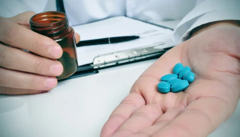 Lekarz podaje kilka niebieskich tabletek, prawdopodobnie ketoprofen, na dłoń.