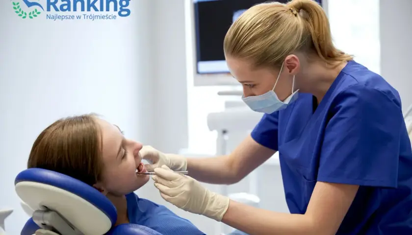 Dentystka w maseczce bada zęby pacjentki w gabinecie stomatologicznym.