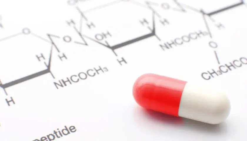 Czerwono-biała kapsułka leży obok wzoru chemicznego. Może to być związane z testem na narkotyki lub badaniami nad nowymi lekami.