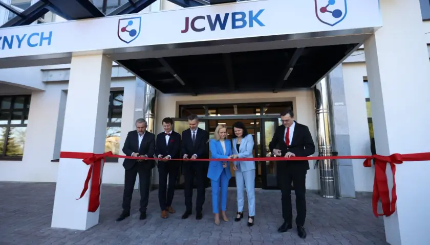 Otwarcie placówki: ludzie przecinają czerwoną wstęgę przed budynkiem z logo JCWBK.