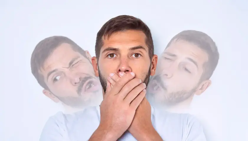Mężczyzna z zespołem Tourette'a zakrywa usta dłońmi, podczas gdy jego twarz wydaje się rozmyta i wykrzywiona w mimowolnych ruchach.