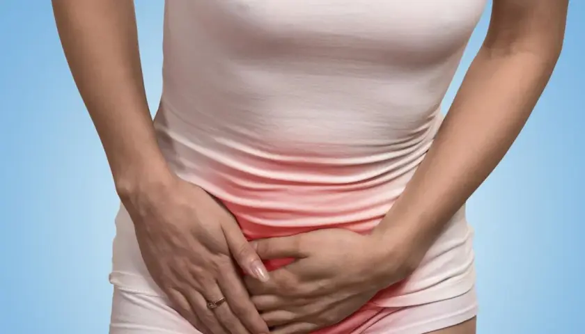 Kobieta trzyma się za brzuch, odczuwając ból w pachwinie. Czerwony obszar na jej ubraniu sugeruje dyskomfort.